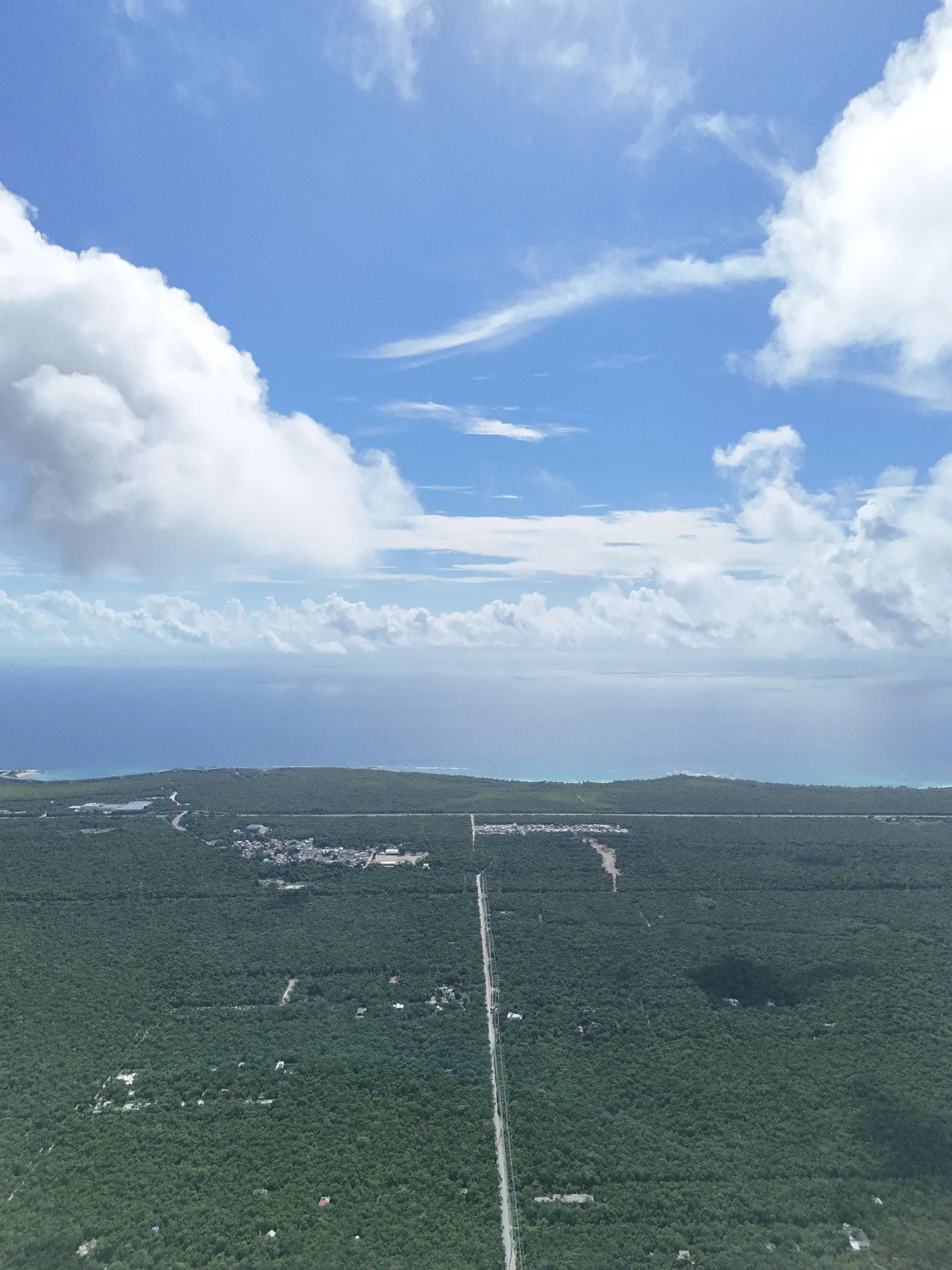 Aerial view east over dense jungle toward the Caribbean, a single road running through and a small town in the distance