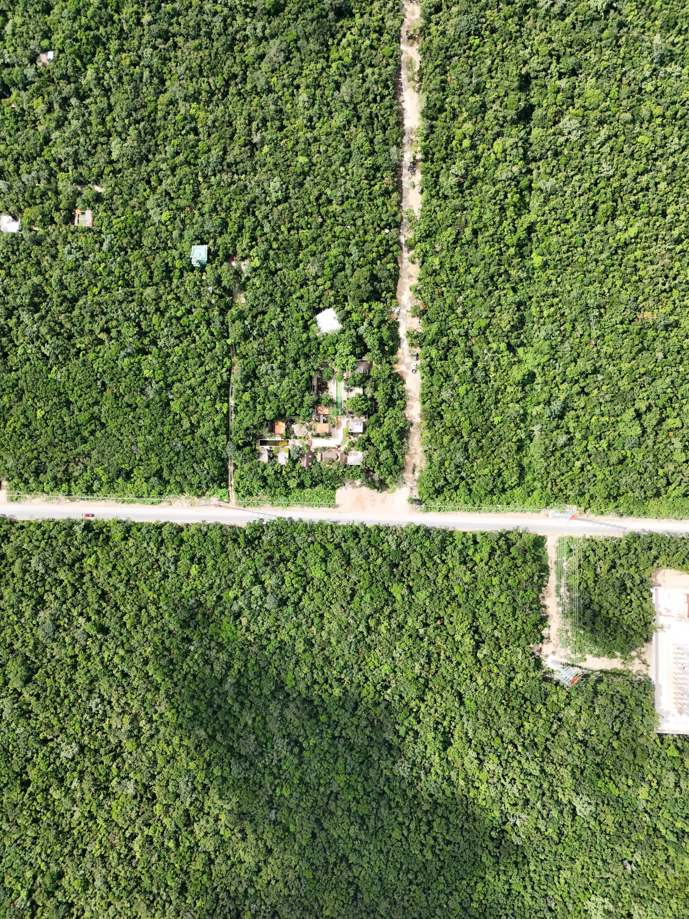 Overhead aerial photograph of a paved road crossing a limestone track, with a small group of houses and a cleared parcel