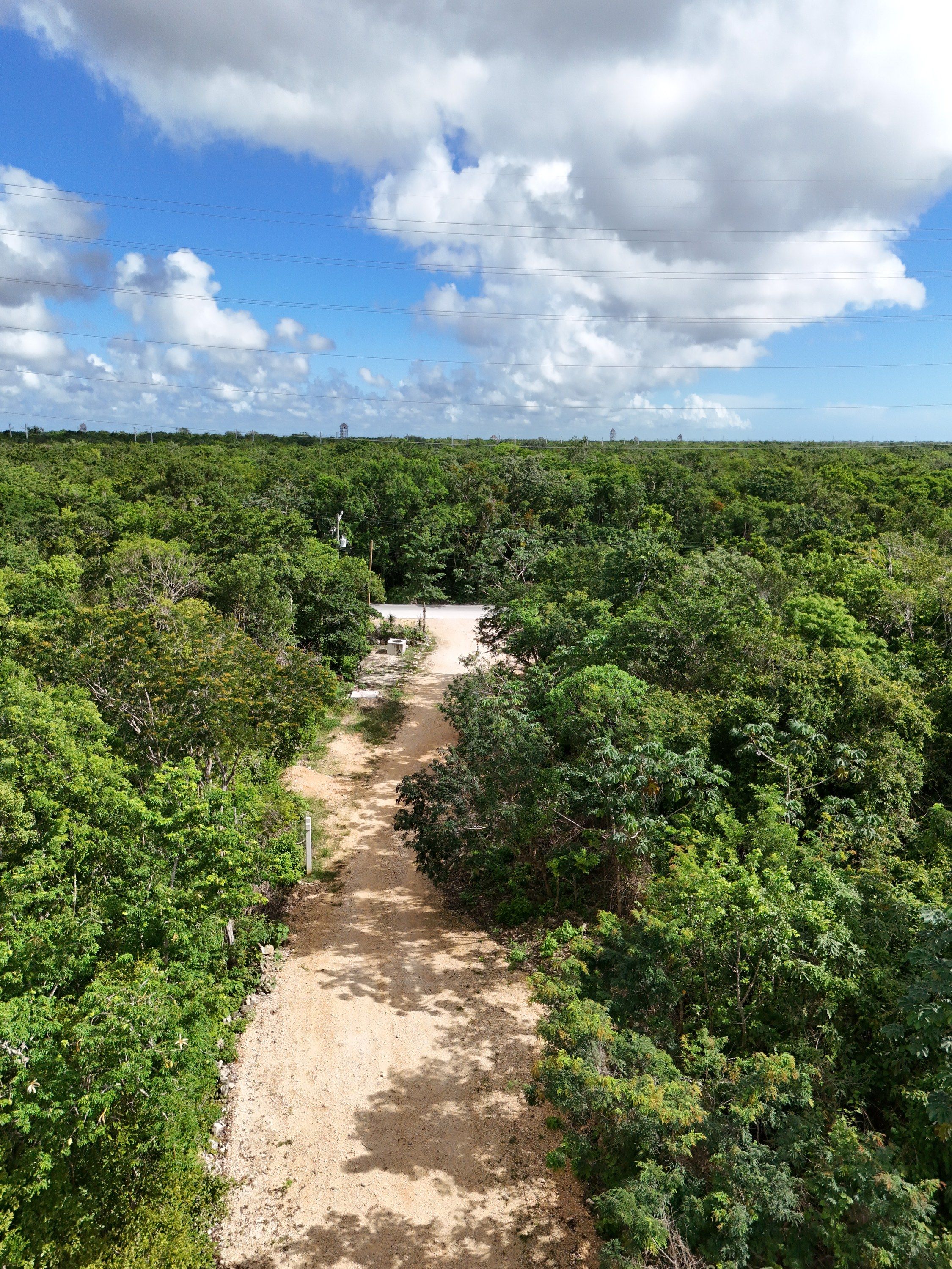 Aerial photograph of a graded limestone track meeting a paved cross road, with high tension power lines overhead
