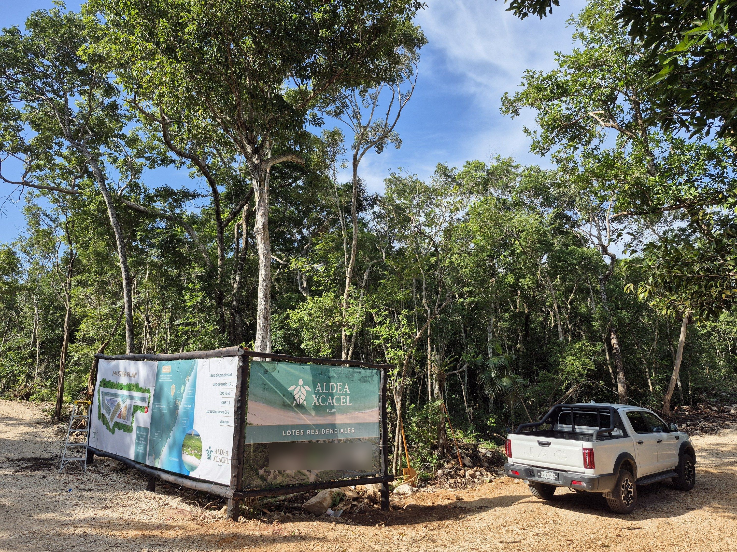 Ground photograph of the project information sign, two banners on a timber frame, standing in a graded limestone clearing with jungle behind it