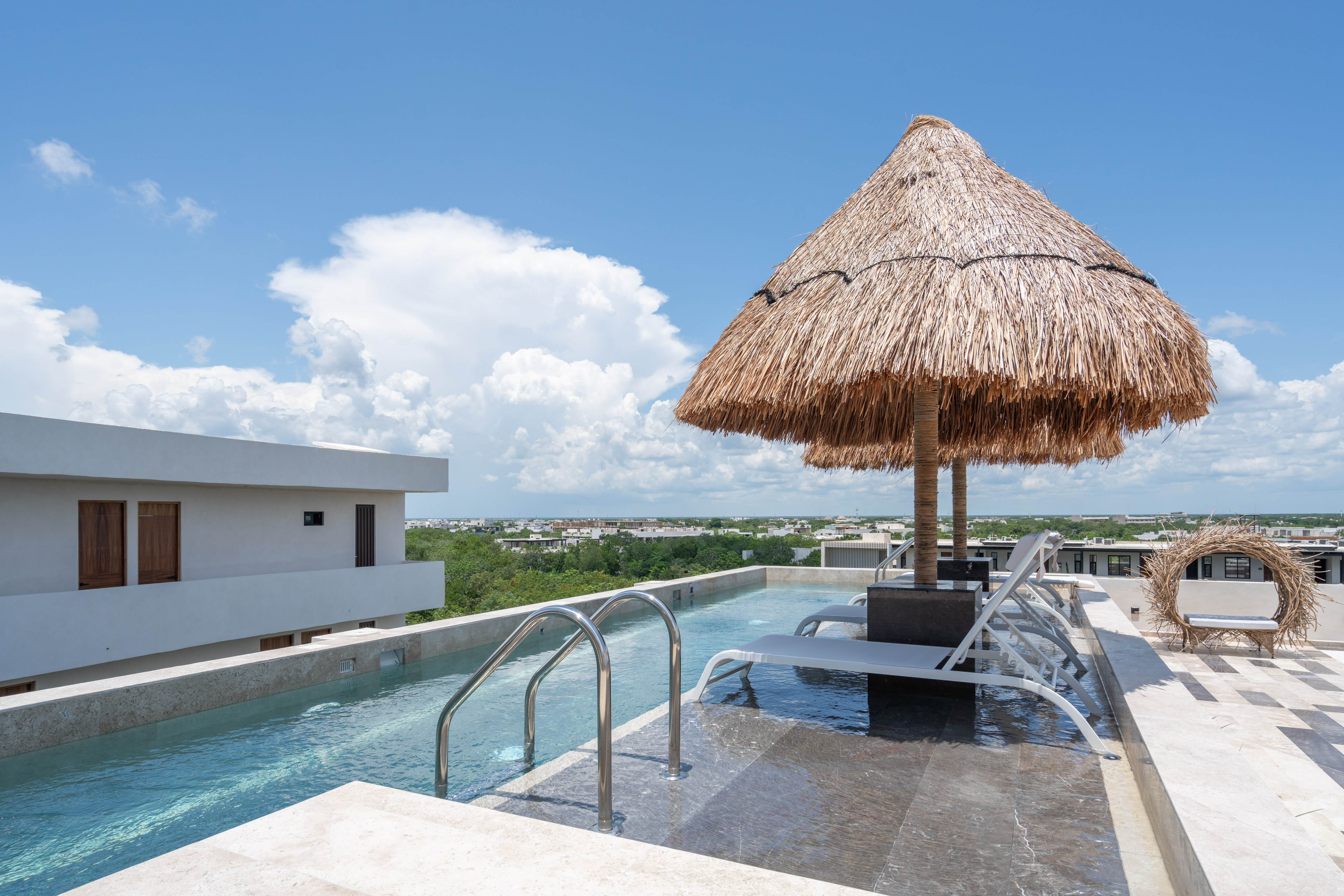 Rooftop infinity pool at Narai with a thatched palapa and Tulum skyline