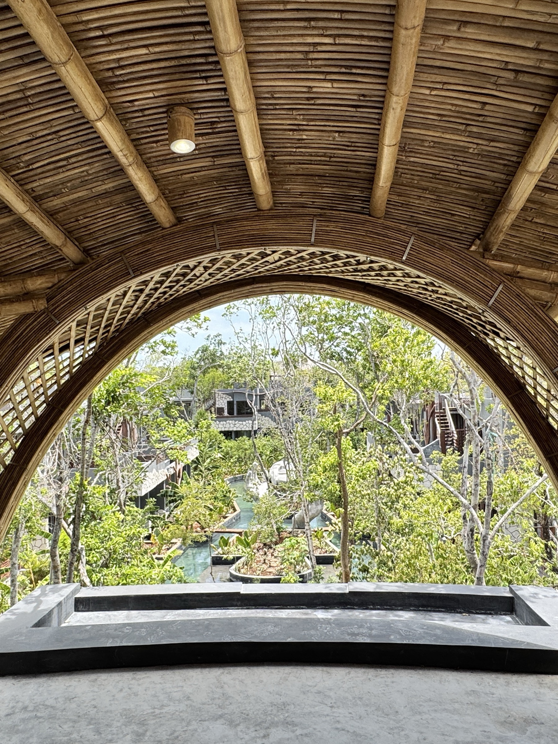 Bamboo-arched pavilion at Siwá Élevé opening onto the canal pools and residential blocks, jungle canopy beyond