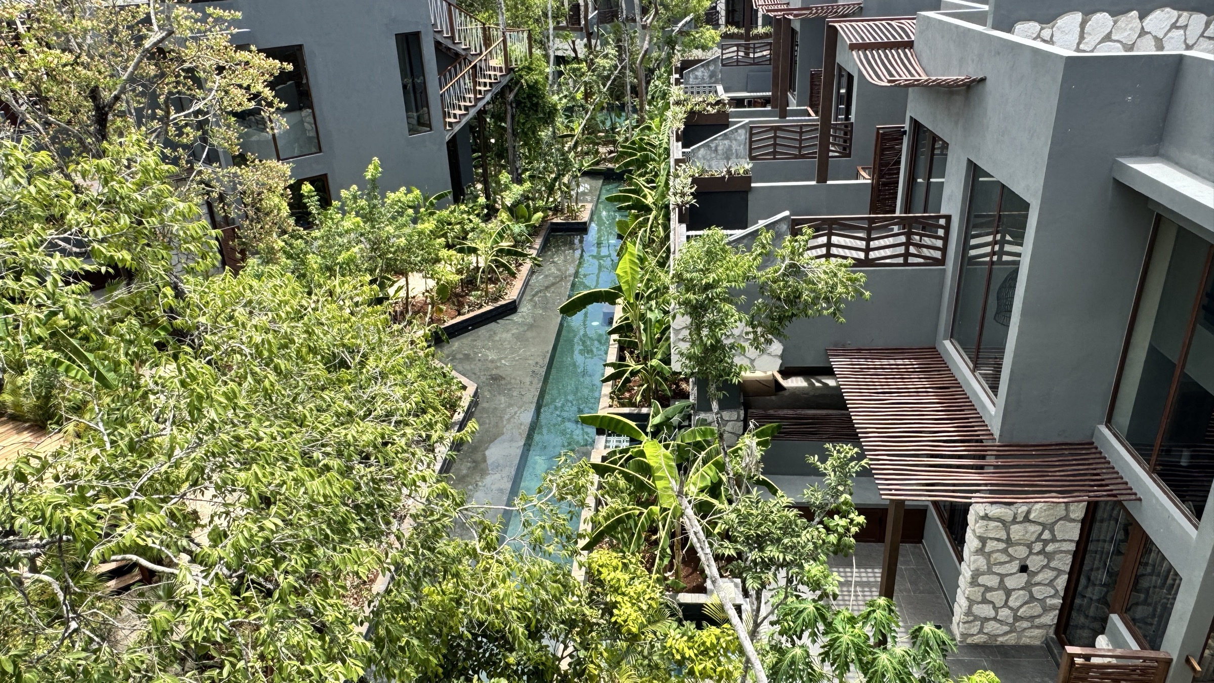 Bamboo-arched pavilion at Siwá Élevé opening onto the canal pools and residential blocks, jungle canopy beyond