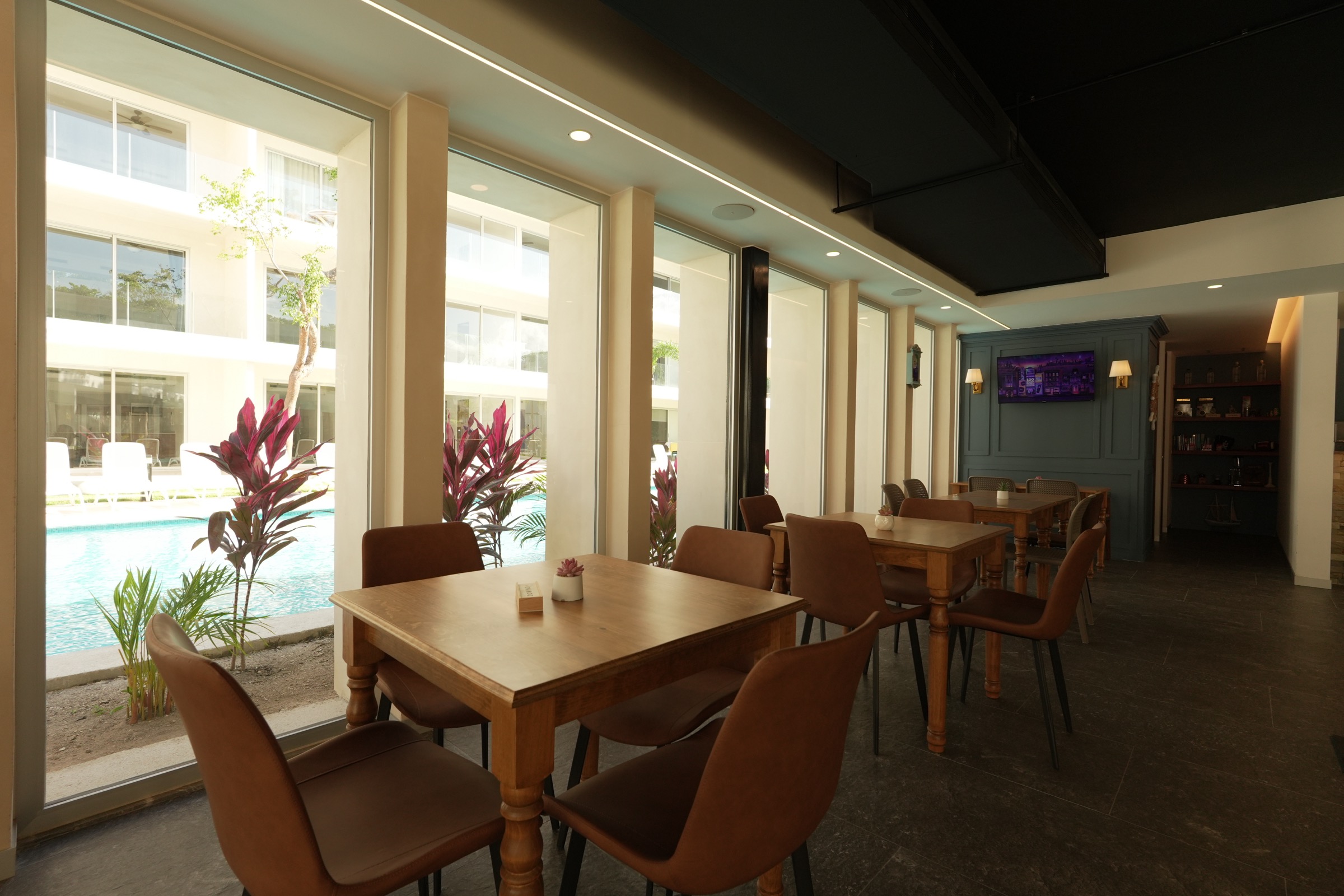 Café inside the clubhouse at The Leaf Condos Playacar with wooden tables against a glass wall onto the pool