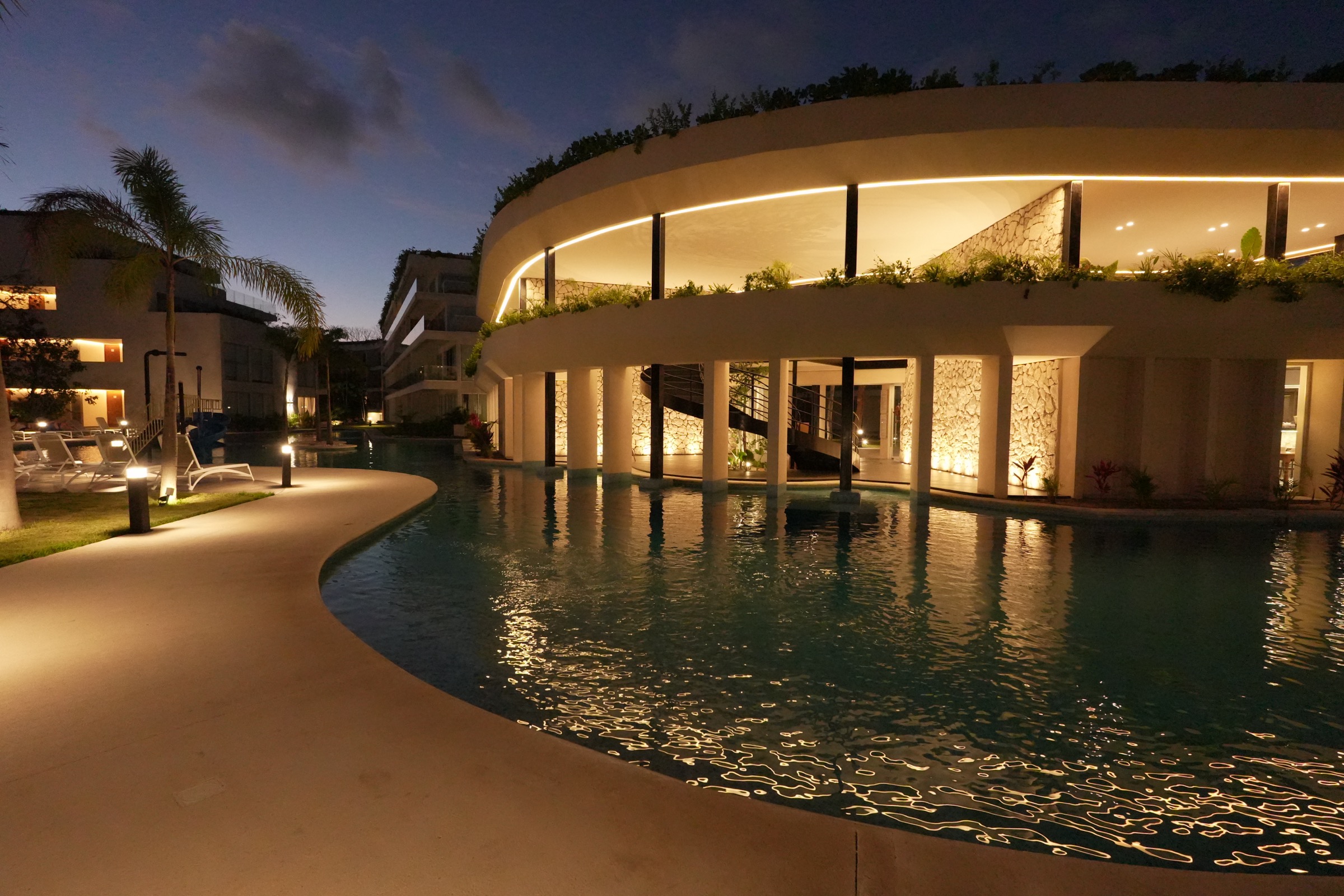 Clubhouse at The Leaf Condos Playacar lit at dusk over the pool