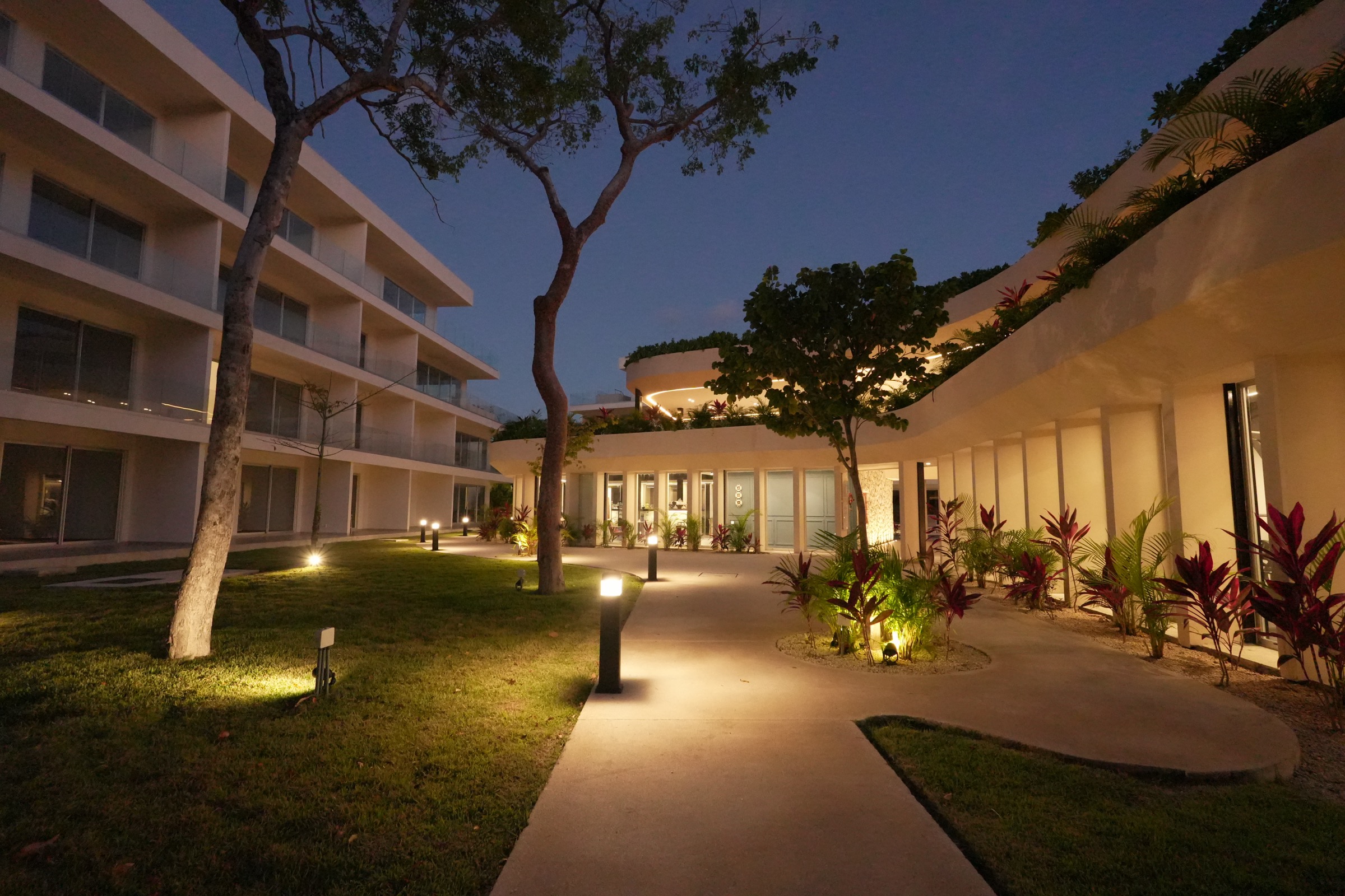 Lit garden walkway between residential wings at The Leaf Condos Playacar at dusk