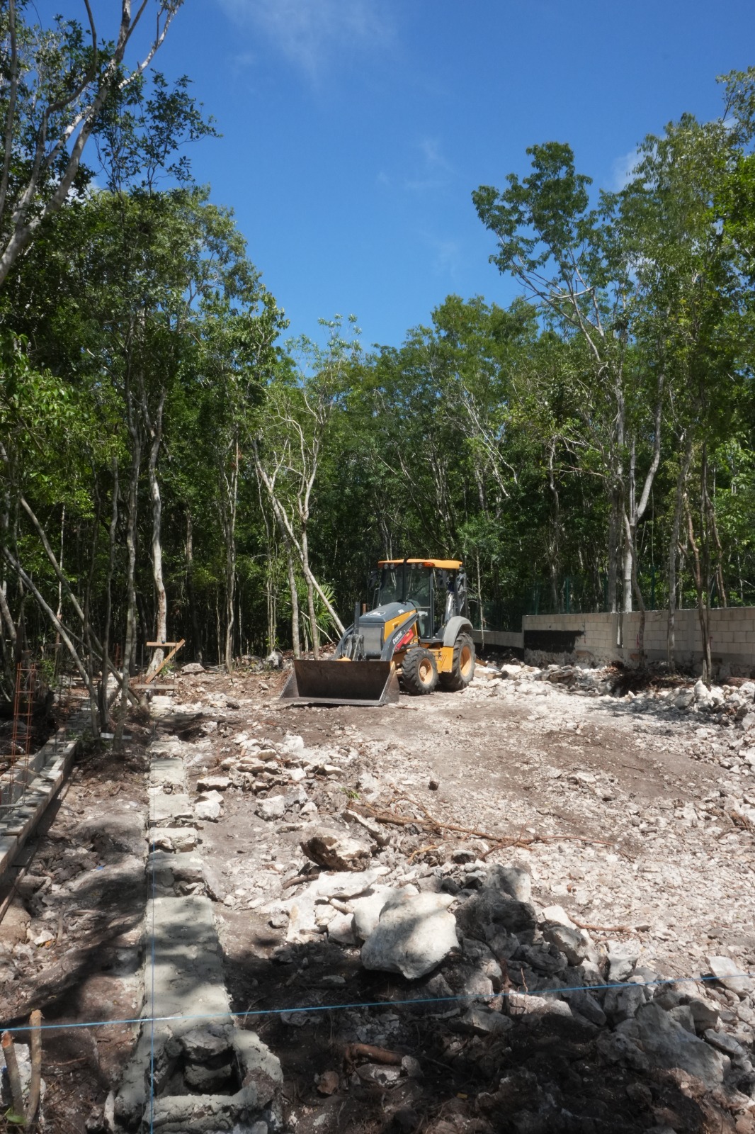 Ground-level photograph of an excavator clearing a raw lot for a house foundation