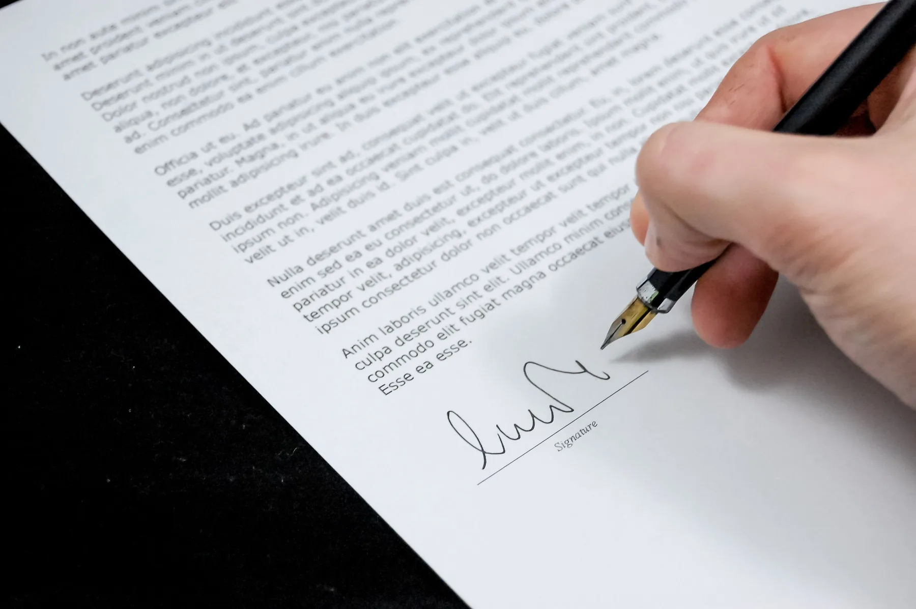 Firma de un documento sobre un escritorio, con pluma y papel
